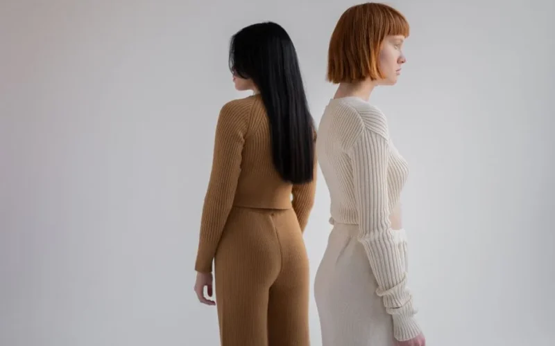 Back view of unrecognizable young female models wearing cozy simple suits while looking away and standing on white background in studio