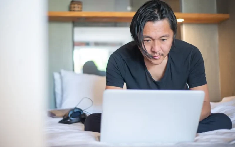 An Asian man working from home on a laptop, focusing on his digital tasks in a cozy indoor setting.