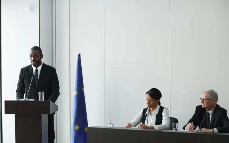 Professional business conference with EU flag, diverse speakers in suits discussing diplomacy.