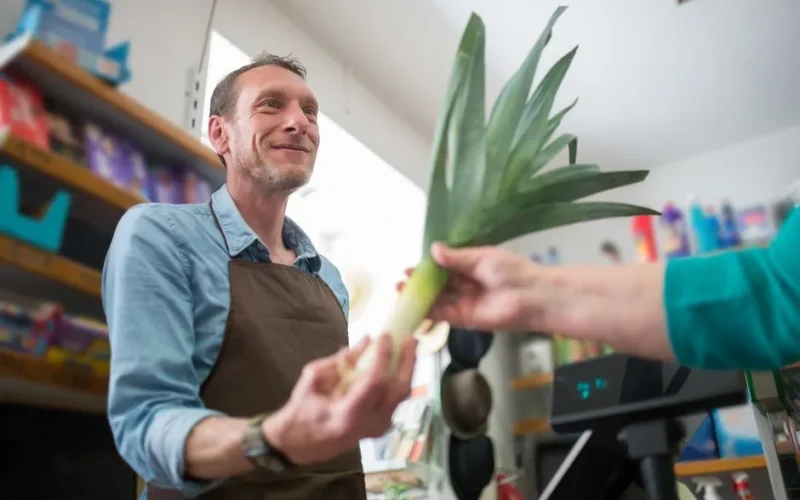 Friendly clerk assisting in vegetable purchase at a grocery store, showcasing personal customer service.