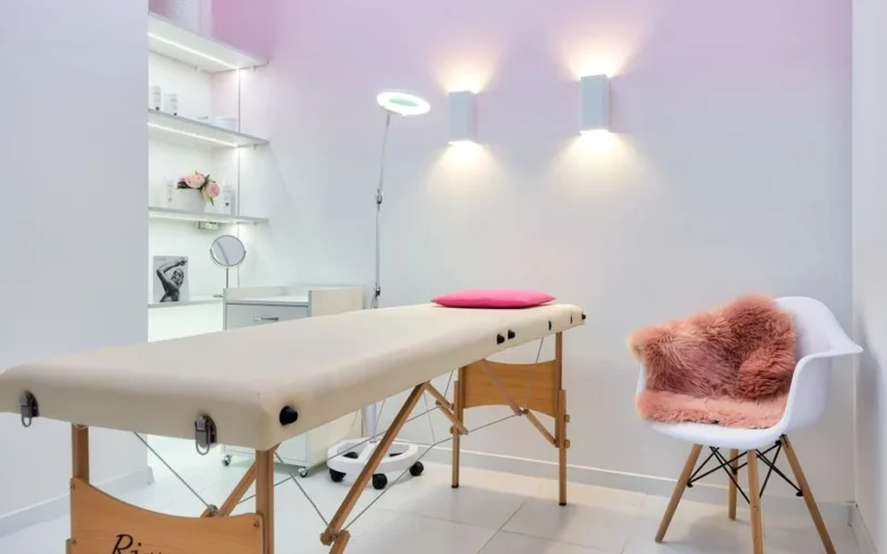 Interior of contemporary workplace of cosmetology salon with couch placed near armchair and shelves with cosmetic products