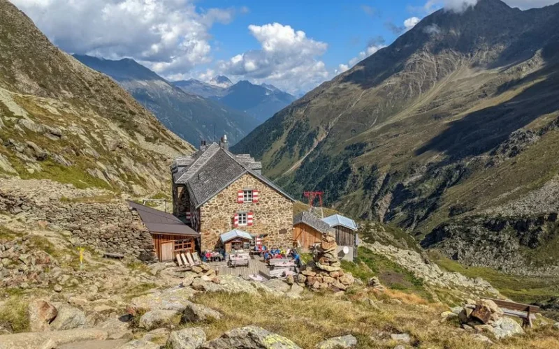 Charming stone hut in the Austrian Alps offers a stunning view of the valley and mountains.