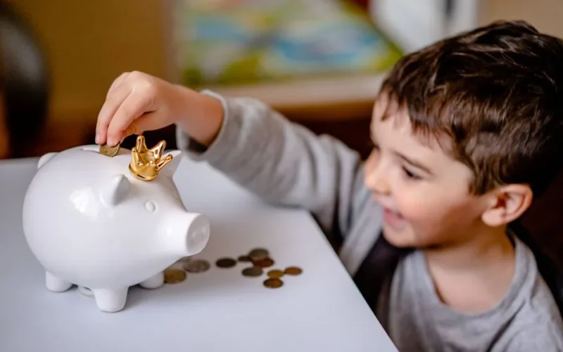 Young boy smiling while saving money in a crowned piggy bank, demonstrating financial responsibility.