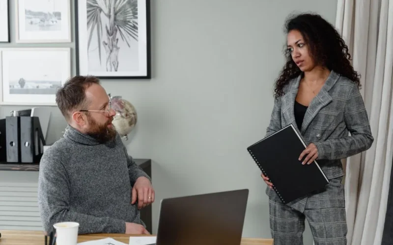A man and woman discuss work in a stylish office environment with modern decor.