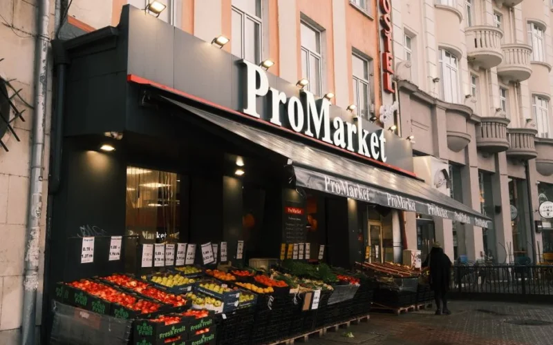 Photo of an urban grocery store, ProMarket, displaying colorful fresh produce outside.