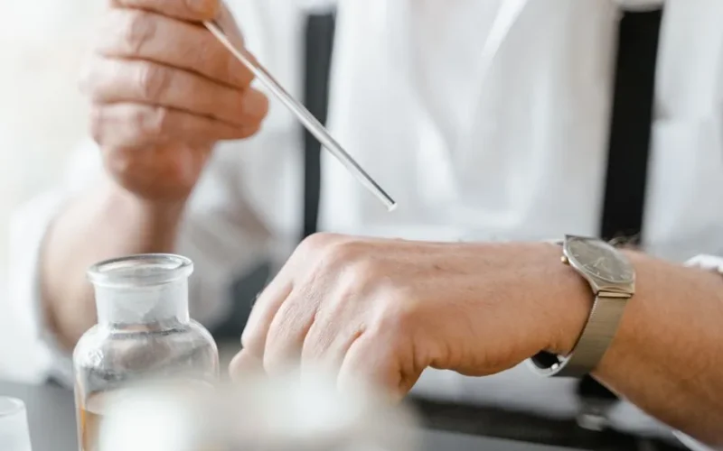 Close-up of a man using a dropper to apply fragrance on his wrist indoors.