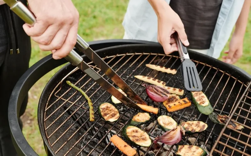 Hands grilling fresh vegetables on a charcoal grill, perfect for a summer picnic outdoors.