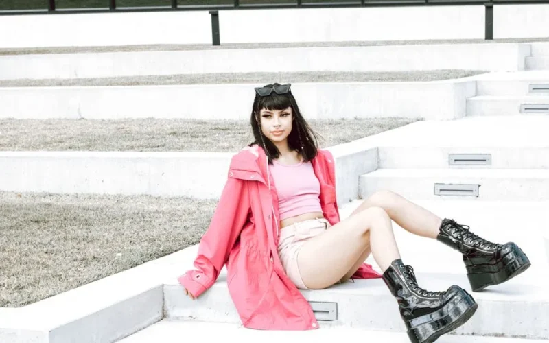 Stylish woman wearing pink jacket and platform boots sitting on outdoor stairs, exuding modern fashion.