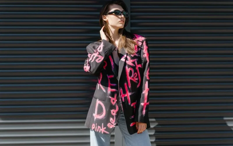 Stylish woman wearing sunglasses and graffiti blazer posing outdoors. Trendy street style fashion.