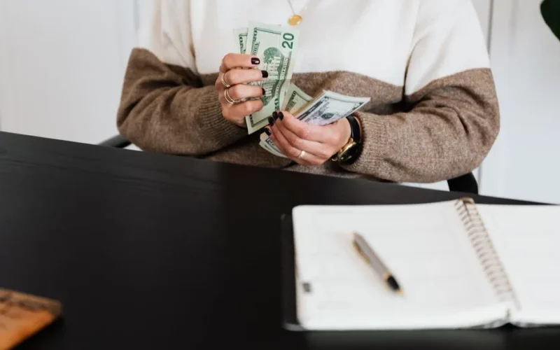 Close-up of an adult counting dollar bills at a desk with a notebook.