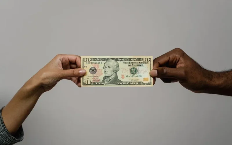 Close-up of two hands exchanging a ten dollar bill, symbolizing financial transaction or exchange.