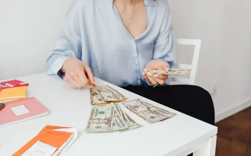 A woman counts US dollar bills at a desk, symbolizing finance management.