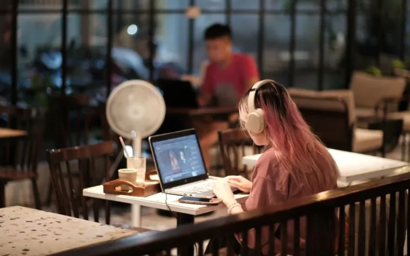 A woman with headphones edits a video on her laptop in a cozy café environment, Vietnam.