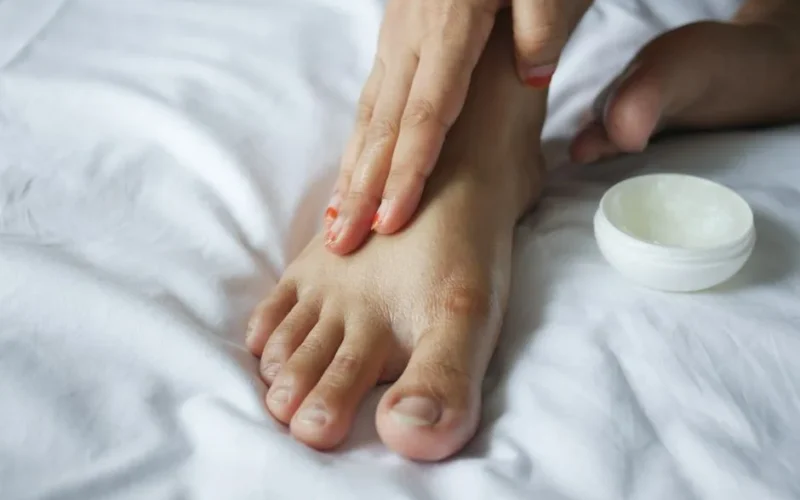 Close-up of a person applying moisturizer to their foot, promoting skin care and hygiene.