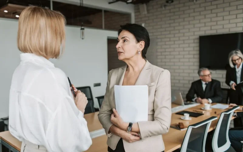Two businesswomen engage in a conversation during a professional meeting in a modern office.
