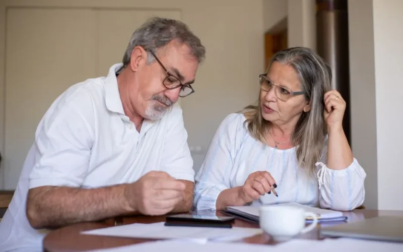 Senior couple reviewing documents and managing finances together at home, showing collaboration and care.