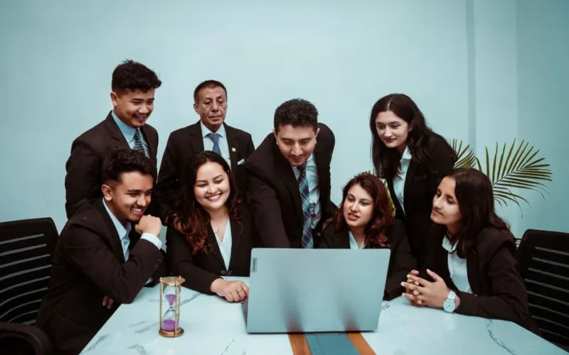 A diverse team of professionals collaborating around a laptop in a modern office setting.