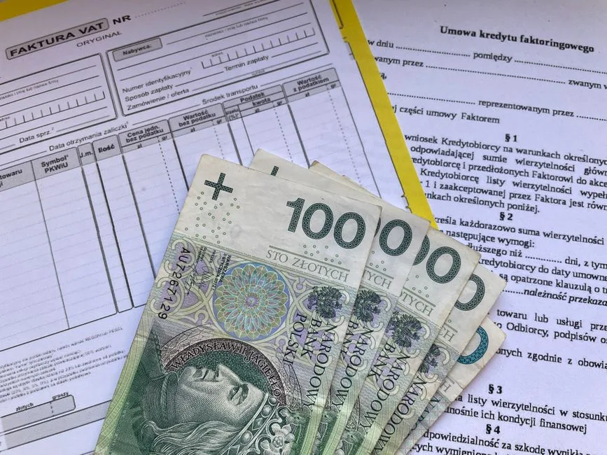 Polish 100 Zloty banknotes on VAT invoice and factoring agreement forms.