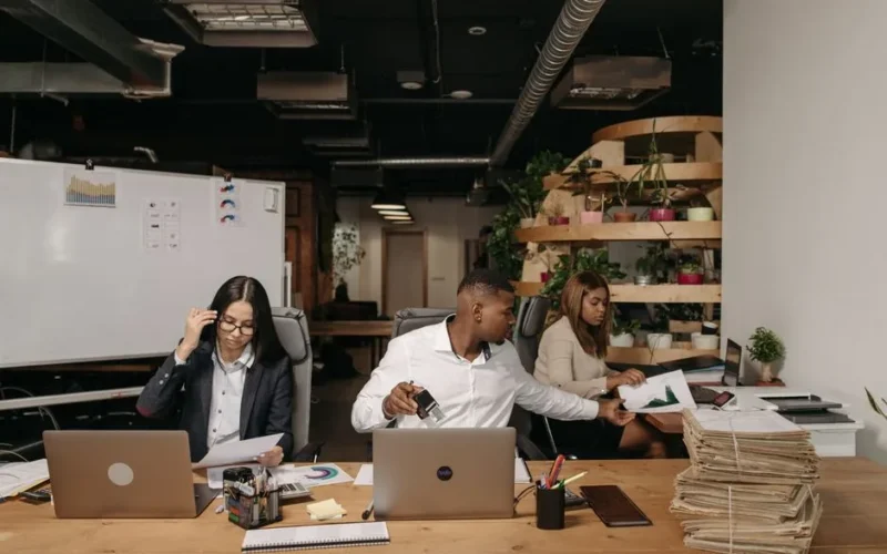 Diverse team collaborating in a modern office setting with laptops and documents.