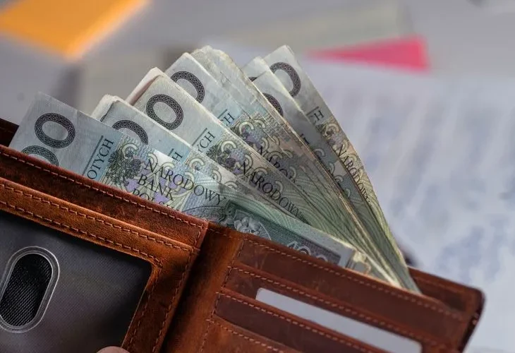 Brown leather wallet containing Polish zloty banknotes on cluttered desk