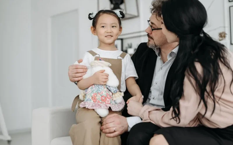A joyful family scene with adopted child cuddling a stuffed toy indoor setting.