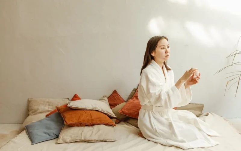 Asian woman practicing a calming skincare routine indoors with soft natural lighting.