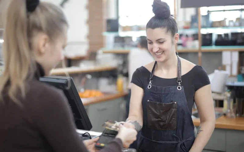 Smiling cashier helping customer with payment at store counter.