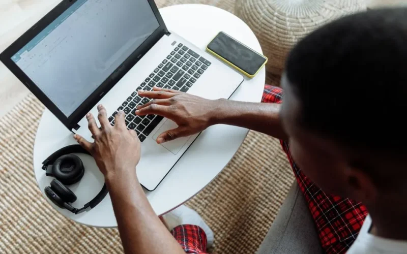 Top view of a man typing on a laptop, with a smartphone and headphones on the desk.