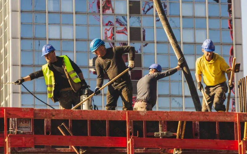 A group of construction workers in safety gear actively working on a high-rise building site.