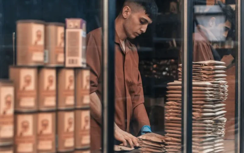 A man packing goods behind a glass window, showcasing a work environment with reflections and stacked items.