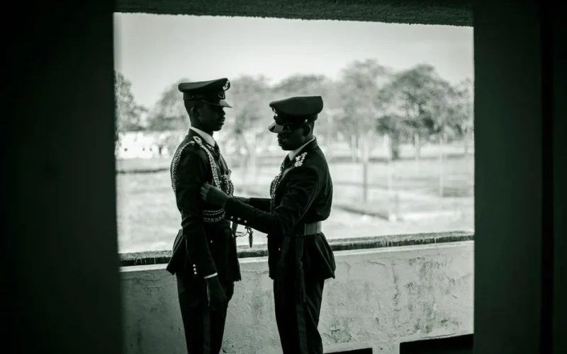 Two soldiers in uniform assisting each other in an outdoor setting. Military camaraderie scene.